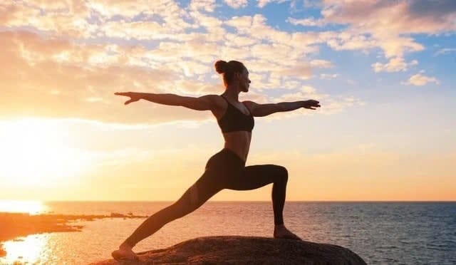 "A girl practicing yoga facing the beach, with the sunset in the background."