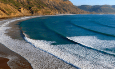 "View of Imsouane beach with its waves and majestic mountains in the background."