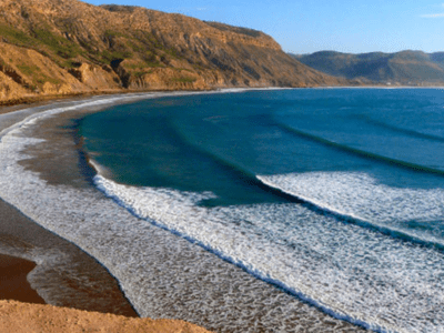 "View of Imsouane beach with its waves and majestic mountains in the background."